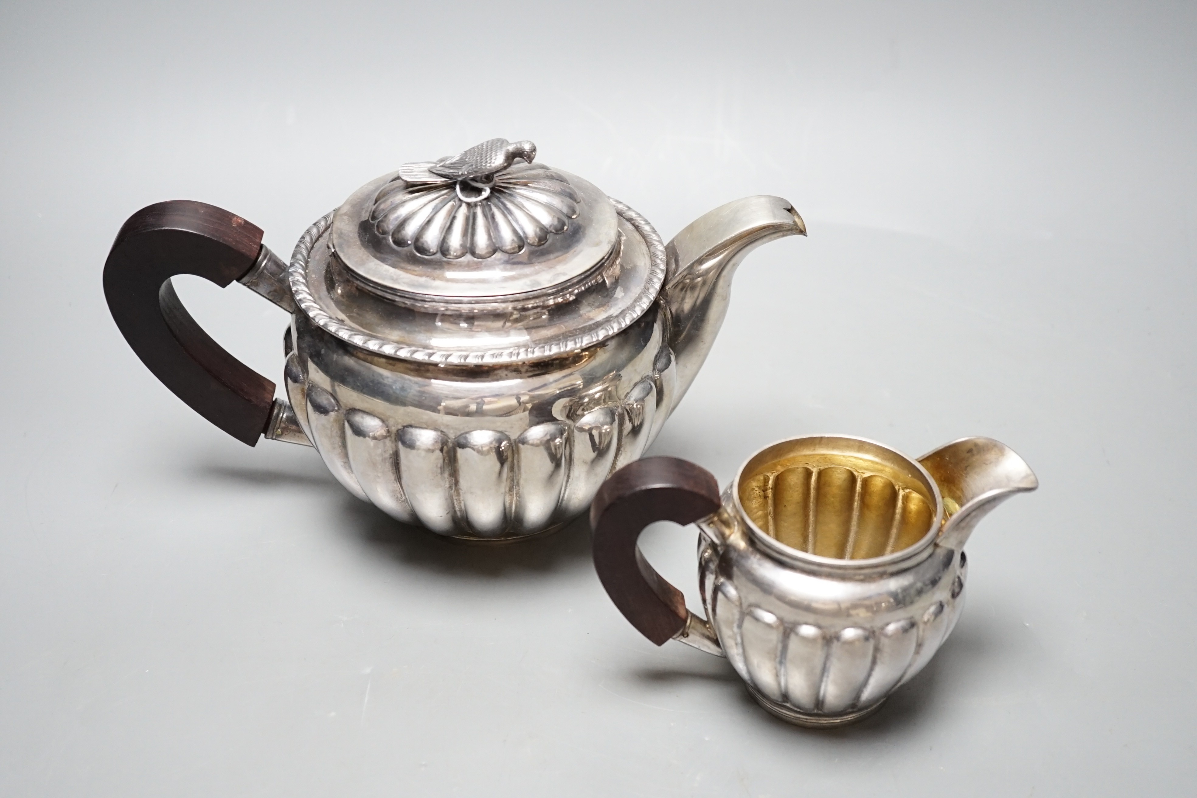 A Chinese Straits? demi fluted white metal teapot and cream jug, with rosewood handles and bird finial, maker TAI, gross weight 31.5oz.